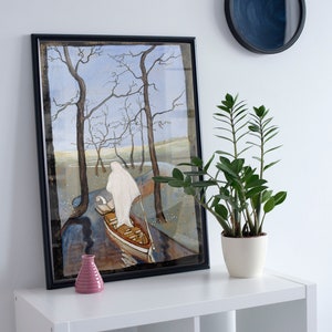 May include: A framed painting of a person in a white robe rowing a boat through a forest. The painting is in a black frame and is hanging on a white wall. A potted plant is on a white shelf below the painting.