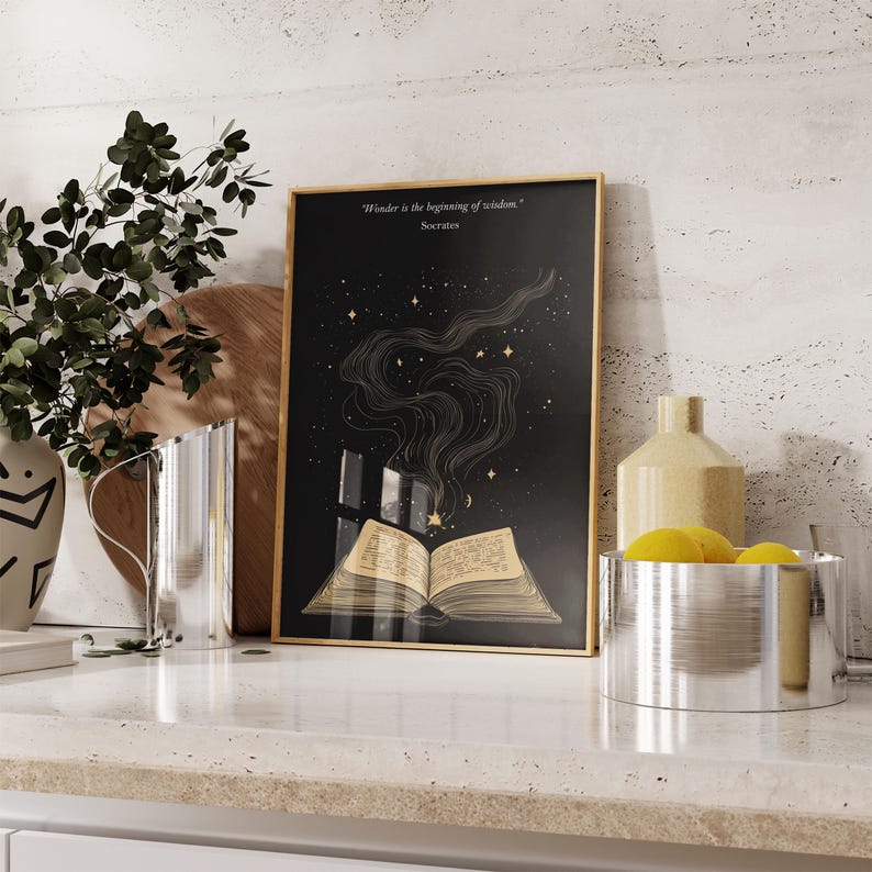 May include: A black and gold framed print with a quote by Socrates: "Wonder is the beginning of wisdom." The print features a stylized illustration of an open book with stars and smoke rising from it.