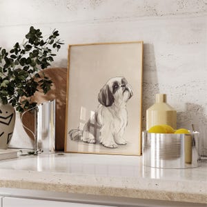 May include: A framed illustration of a white and brown Shih Tzu dog sitting and looking up. The dog is in a light brown frame on a white countertop.