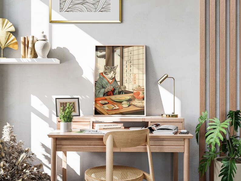 Puede incluir: Una impresi&oacute;n enmarcada de un gato con un kimono y sosteniendo palillos, sentado en una mesa con un taz&oacute;n de comida y una tetera. La impresi&oacute;n est&aacute; en un escritorio de madera con una l&aacute;mpara, libros y plantas.