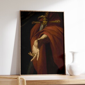 May include: A close-up of a painting depicting a hand holding a sword with a gold hilt. The hand is wearing a red robe.