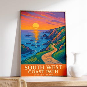 May include: A framed art print featuring a coastal landscape with a sunset. The artwork depicts a path winding along a cliffside, overlooking the ocean. The text "SOUTH WEST COAST PATH UNITED KINGDOM" is displayed at the bottom.