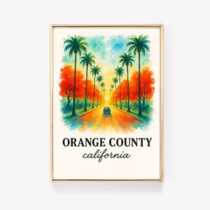 May include: Watercolor print of a road lined with palm trees and orange trees, with a car driving towards the sun. The text "ORANGE COUNTY california" is at the bottom of the print. The print is in a gold frame.