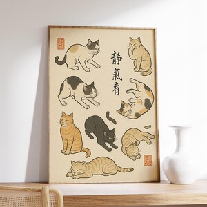 Op de afbeelding: Een ingelijste print met gestileerde illustraties van verschillende katten in verschillende poses. De katten zijn afgebeeld in een minimalistische stijl met zwarte contouren en gevuld met neutrale kleuren. Japanse tekst is aanwezig.