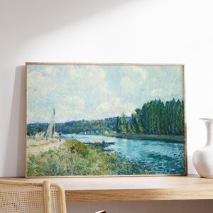 May include: A framed painting depicting a river scene with a sailboat in the foreground, a lush green forest on the opposite bank, and a blue sky with white clouds.