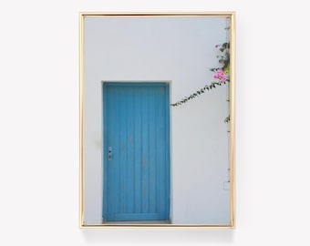 Peut inclure: Photographie encadrée d'une porte bleue vive sur un mur blanc. Une plante grimpante avec des fleurs roses ajoute une touche de couleur. Le cadre doré rehausse l'esthétique de l'image, créant une ambiance méditerranéenne.