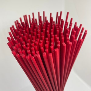 May include: A bundle of red wooden diffuser sticks. The sticks are arranged in a circular pattern, with the ends of the sticks pointing towards the center.