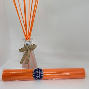 May include: A set of orange diffuser reeds in a clear glass bottle with a silver cap and a brown bow. The reeds are also packaged in a clear plastic bag with a label that says "Diffuser Reeds" in blue text.