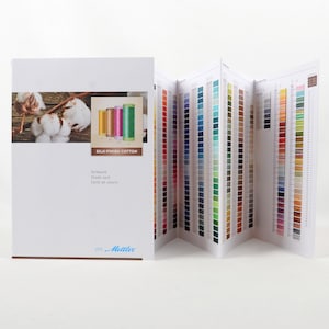 May include: A white booklet with a color chart of silk-finish cotton thread. The booklet is open, revealing a fan of thread color samples. The cover features cotton bolls and spools of thread. The text "SILK-FINISH COTTON" is visible.