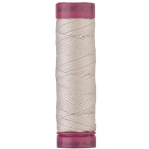 May include: A spool of light beige sewing thread wrapped around a cylindrical core with magenta plastic ends. The top end features the text AMANN GROUP, and the bottom end displays the text Polyester No. 38. The thread has a smooth texture.