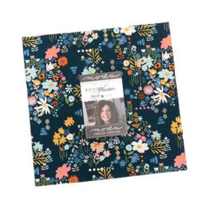 May include: A square fabric bundle with a dark blue floral pattern featuring white, pink, orange, and yellow flowers. A small card with the text "moda BOHO Haven" and a woman's photo is on top. The fabric is likely for quilting or sewing projects.
