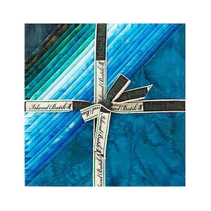 May include: A square stack of fabric squares featuring a gradient of blue and green batik patterns. The stack is tied with a white ribbon printed with the text Island Batik in a repeating pattern, securing the fabric layers in a neat bundle.