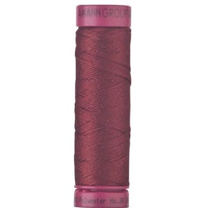 May include: A spool of dark burgundy sewing thread with magenta plastic end caps. The top cap is embossed with the text AMANN GROUP, and the bottom cap features the text Polyester No. 30. The thread is wound in a cross-hatch pattern.