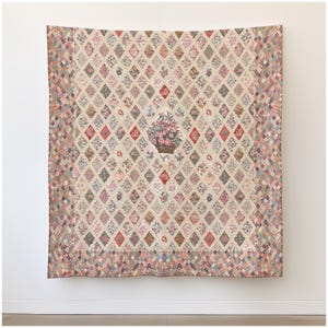 May include: A large, vintage quilt with a diamond pattern. Each diamond features a floral design in various colors, including pink, red, and blue. A central diamond showcases a basket of flowers. The quilt has a neutral background and a patterned border.