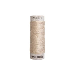 May include: A spool of Aurifil thread, beige in color, with the text "AURIFIL" printed on the top and "MADE IN ITALY" on the bottom. The thread is tightly wound around a cardboard core, ideal for sewing and quilting projects.