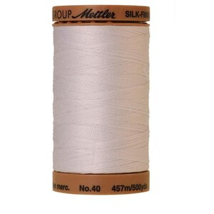 May include: A spool of white Mettler Silk-Finish thread with the text "GROUP Mettler SILK-FINISH" on the top and "No. 40 457m/500yds" on the bottom.