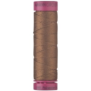 May include: A spool of brown sewing thread with magenta plastic end caps. The top cap is printed with the text AMANN GROUP, and the bottom cap features the text 100% Polyester. The thread is wound in a cross-hatch pattern around the central cylinder.