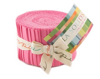 May include: A pink fabric roll with a white ribbon tied around it. The label on the roll reads "La Solids Moda".