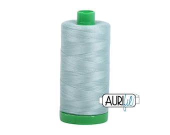 May include: A spool of light blue thread with a green base and top. The thread is tightly wound, and the spool has the Aurifil logo on the side. This thread is likely used for sewing or embroidery projects.