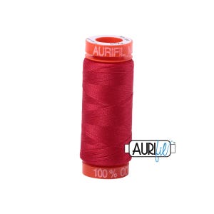 May include: A spool of red Aurifil cotton thread. The spool has a red body and a bright orange top and bottom. The text "AURIFIL" is printed on the top of the spool. The bottom of the spool reads "100% CO".
