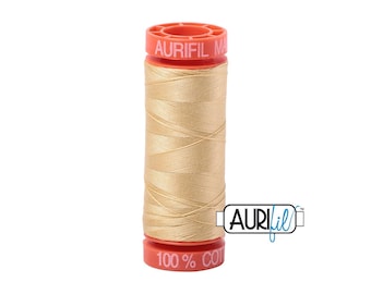 May include: A spool of Aurifil thread in a light tan color. The spool has a red top and bottom with the brand name and "100% COT" printed on it. The thread is tightly wound around the spool, ready for sewing projects.