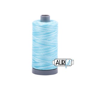 May include: A spool of Aurifil thread in a light blue and white variegated color. The thread is wound around a gray plastic spool. The Aurifil logo is visible on the side of the spool.