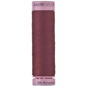 May include: A cylindrical spool of dark burgundy sewing thread with light pink plastic caps at the top and bottom. The top cap features the text AMANN GROUP and the bottom cap displays the text 100% Polyester in black lettering.