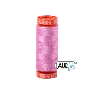 May include: A spool of light pink Aurifil 100% cotton thread. The spool has an orange top and bottom with the brand name and thread details printed on it. The thread is tightly wound and ready for sewing projects.