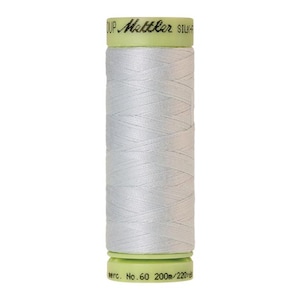 May include: A spool of white silk thread. The thread is tightly wound around a cylindrical core. The spool has a light green top and bottom with the brand name "Mettler Silk-Finish" printed on it. The thread is mercerized, No. 60, and 220 yards.