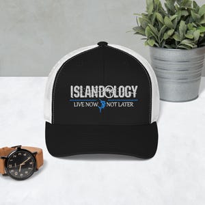 Puede incluir: Gorra de camionero negra y blanca con la palabra "ISLANDOLOGY" en letras blancas. La gorra tiene una visera negra y una parte trasera de malla blanca. El texto "LIVE NOW NOT LATER" está debajo, con un gráfico azul.