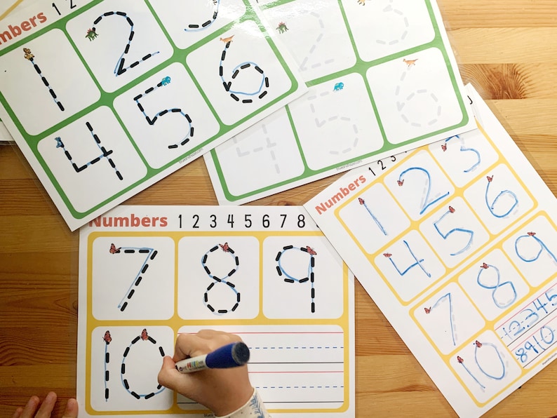 May include: A child's hand traces the number 10 on a yellow and white worksheet with black dotted lines. The worksheet has the title "Numbers 1 2 3 4 5 6 7 8" and includes other numbers with dotted lines for tracing.