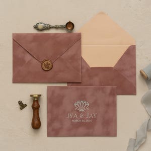 a pink envelope with a wax seal, a wooden clip, and a ribbon, all arranged on a light-colored surface.