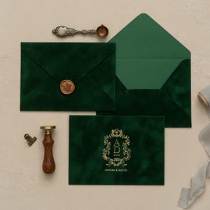 a collection of green velvet envelopes, a wooden seal, and a gold-colored metal stamp, all arranged on a light-colored surface.