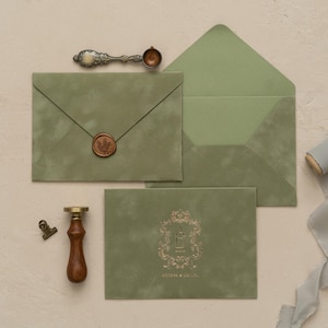 a collection of green envelopes, a wooden seal, a brass clip, and a ribbon, all arranged on a light-colored surface.
