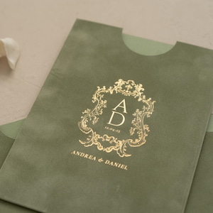 A close-up of a green envelope with a gold embossed logo that reads "ANDREA & DANIEL" and "12.05.20".