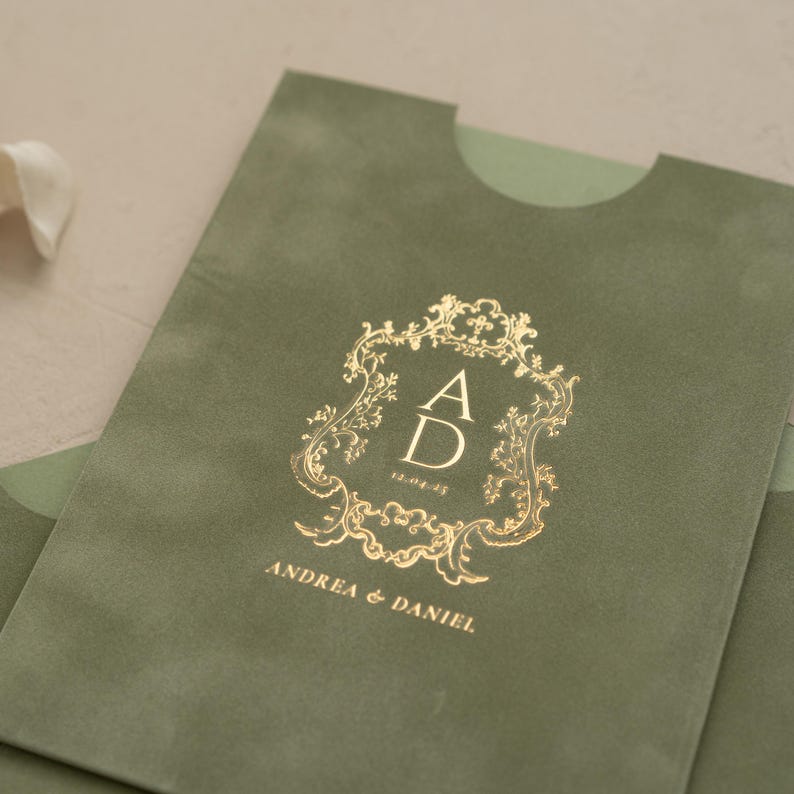 A close-up of a green envelope with a gold embossed logo that reads "ANDREA & DANIEL" and "12.05.20".