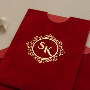 A close-up image of a red velvet envelope with a gold decorative border and the letters 'SK' prominently displayed in the center.