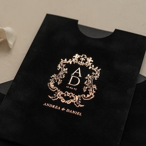 A black envelope with a gold embossed monogram and text, likely a wedding invitation or card.