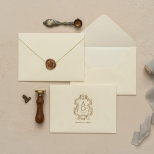 a collection of wedding-related items, including an envelope, a wax seal, a ribbon, and a wooden seal, all arranged on a light-colored surface.