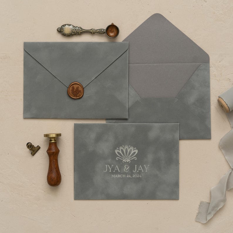 a collection of gray envelopes, a wooden seal, a wax seal, and a ribbon, all arranged on a light-colored surface.