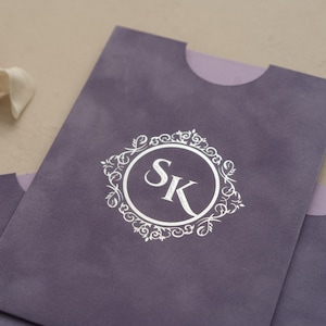 A close-up image of a purple envelope or card with a white circular logo featuring the letters 'SK' in the center.