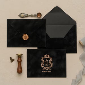 a collection of black envelopes, a wooden wax seal, and a gold-colored wax seal, all arranged on a light-colored surface.