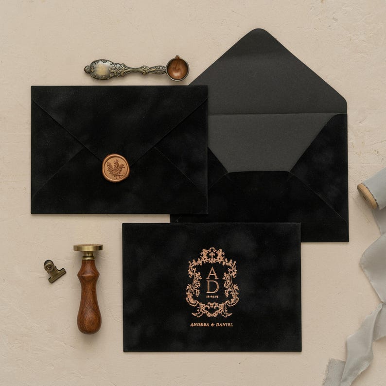 a collection of black envelopes, a wooden wax seal, and a gold-colored wax seal, all arranged on a light-colored surface.