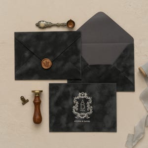 a collection of black envelopes, a wooden seal, a wax seal, and a ribbon, all arranged on a light-colored surface.