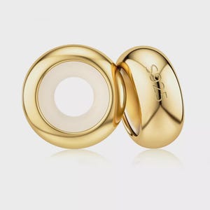 May include: Two gold-toned, smooth, rounded ring-shaped charms. One charm is positioned flat, revealing a white circular centre, while the other is tilted, displaying the engraved text S925 on its polished, reflective, curved outer surface.