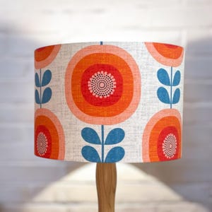 May include: A lampshade with a white background and a repeating pattern of orange, red, and pink circles with blue leaves. The lampshade is made of fabric and has a textured surface.