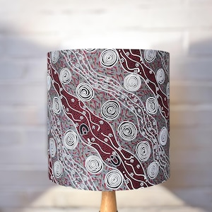 May include: A lampshade with a red, white and grey patterned design. The pattern features circles and lines, reminiscent of Aboriginal art.