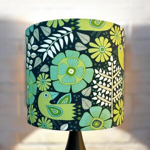 May include: A green and black lampshade with a floral and bird pattern. The lampshade has a white background with green and black flowers and birds.