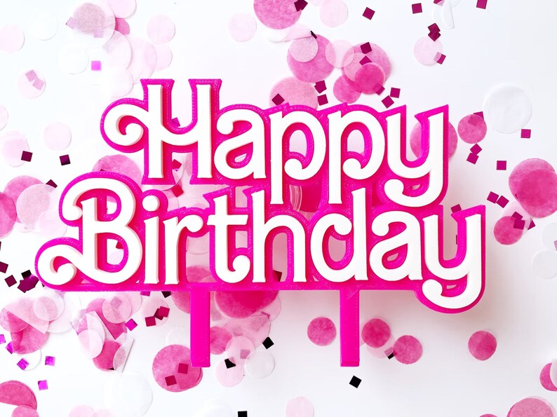May include: A pink and white "Happy Birthday" cake topper with a decorative font. The topper is surrounded by pink confetti on a white background, creating a festive and celebratory atmosphere.