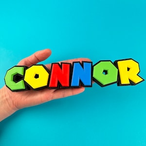 May include: A 3D printed name sign spelling "CONNOR" in colourful block letters. The letters are yellow, red, blue, green, and yellow. The letters are outlined in black.